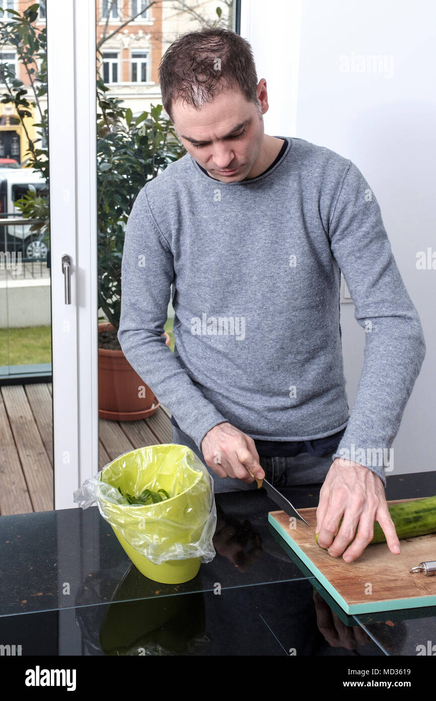Man -40-45 years old, peeling and cutting cucumber in the kitchen Stock Photo