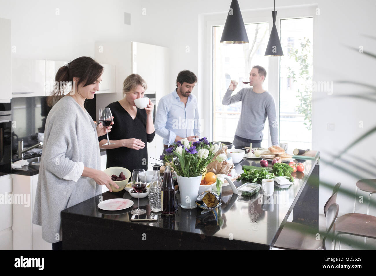 Group of friends  preparing food together.Casually  chatting and snacking on a selection of  vegetarian food while laughing and enjoying themselves in Stock Photo
