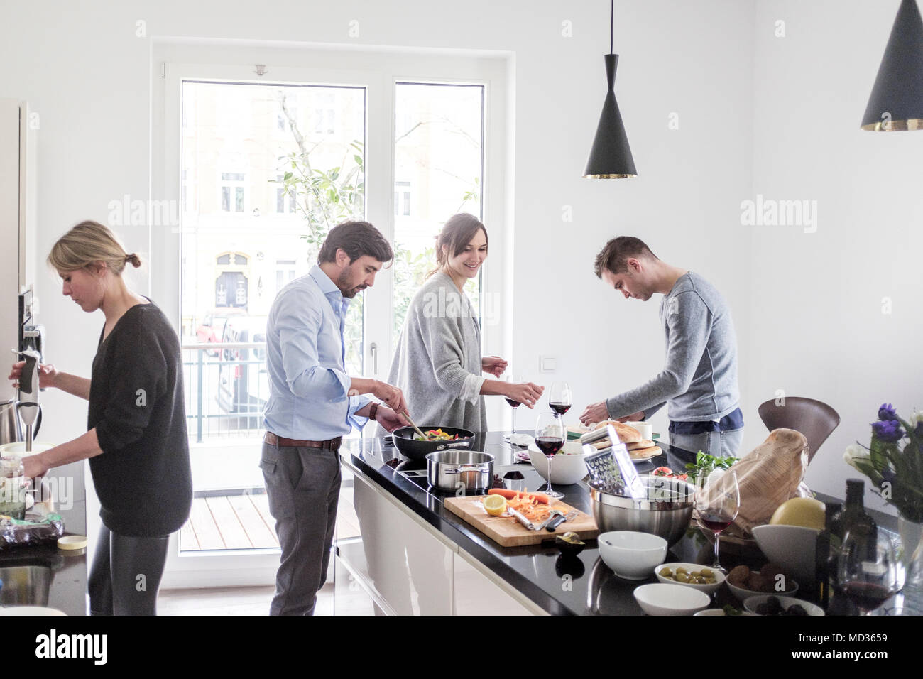 Group of friends casually cooking together while laughing and enjoying themselves. Stock Photo