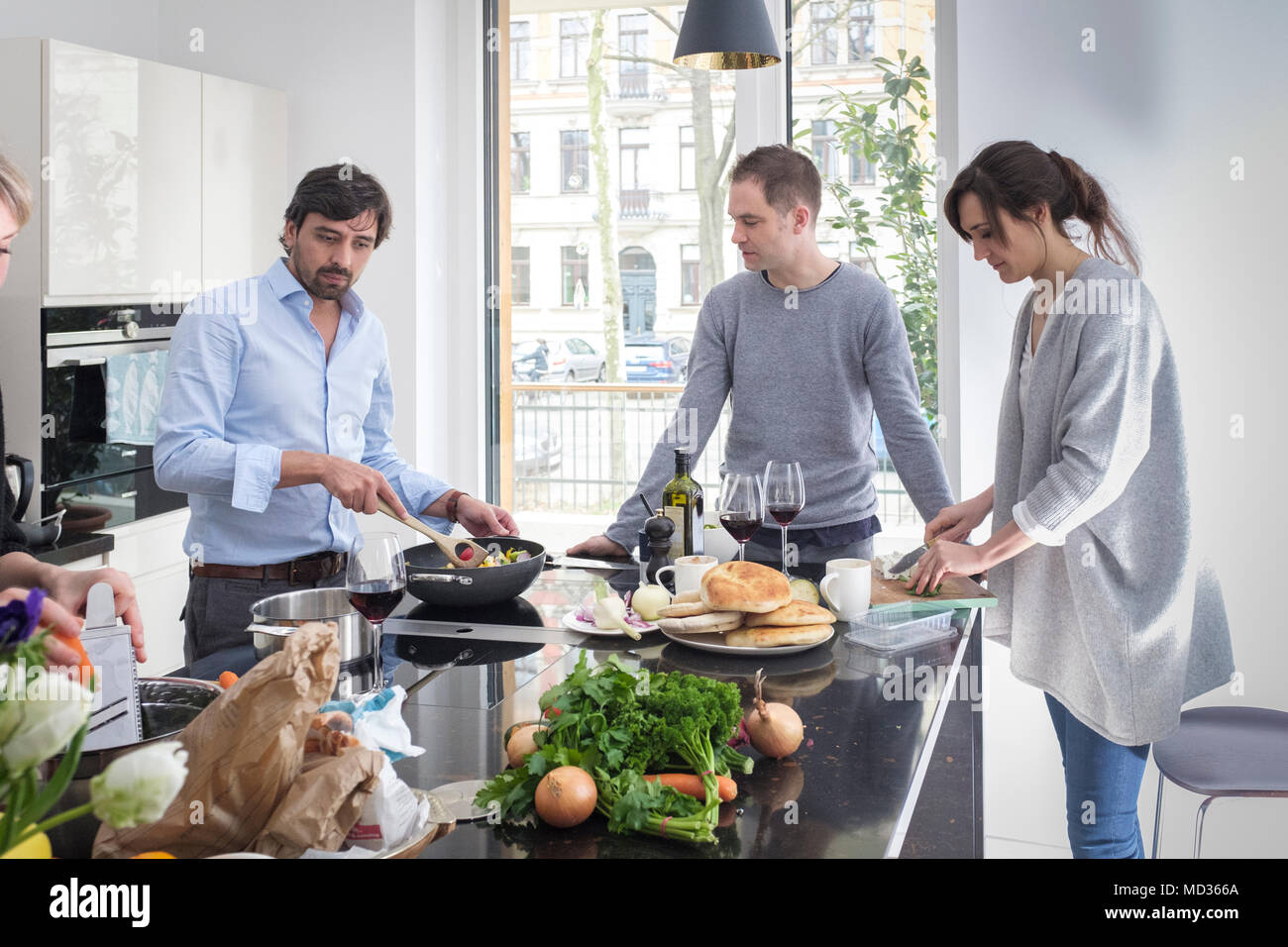 Group of friends preparing vegetarian food together while laughing and enjoying themselves in the kitchen Stock Photo