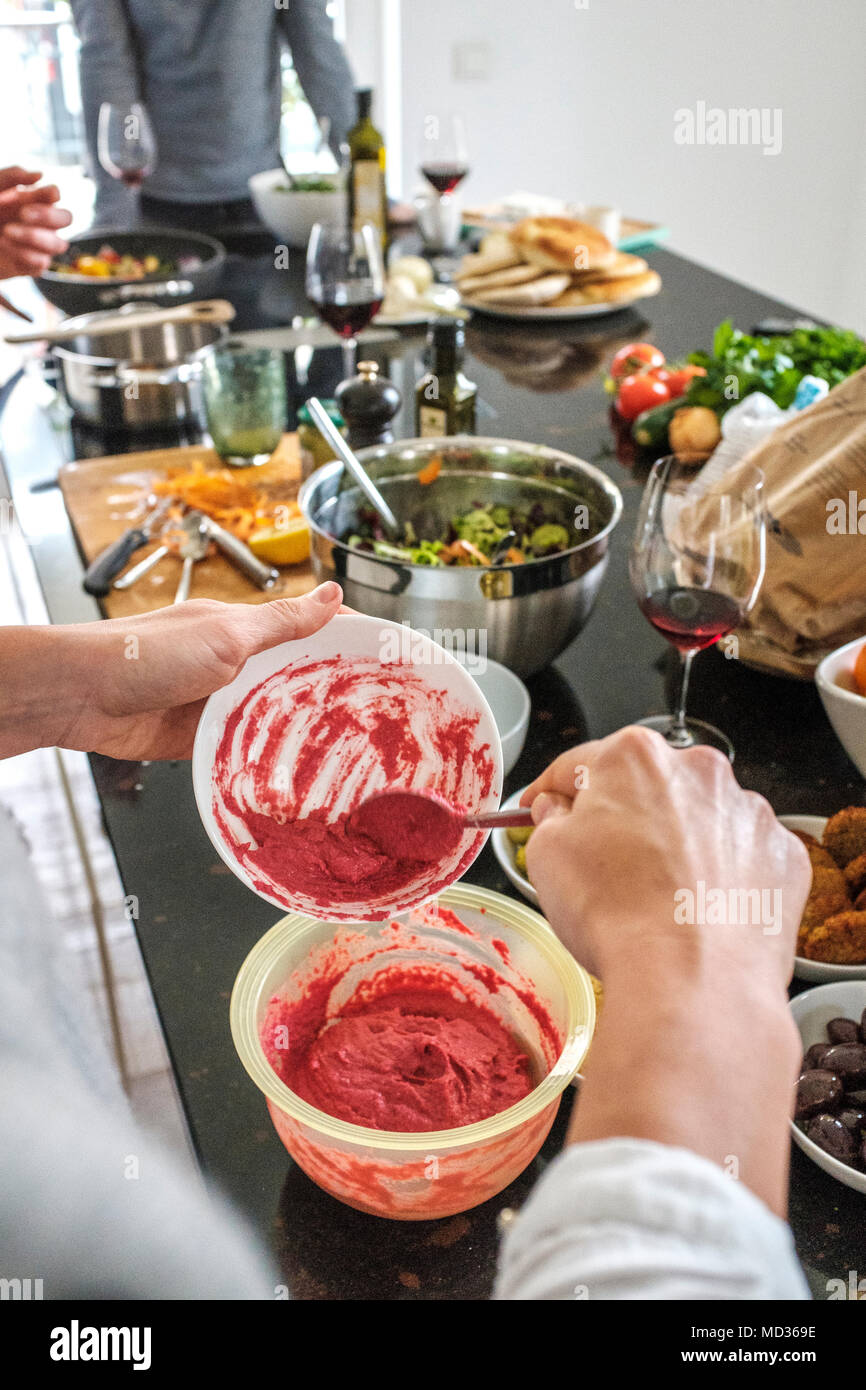 Woman preparing beetroot hummus and selection of vegetarian platers-mixed salad,green olive,hummus classic.Group of friends casually snacking on a sel Stock Photo