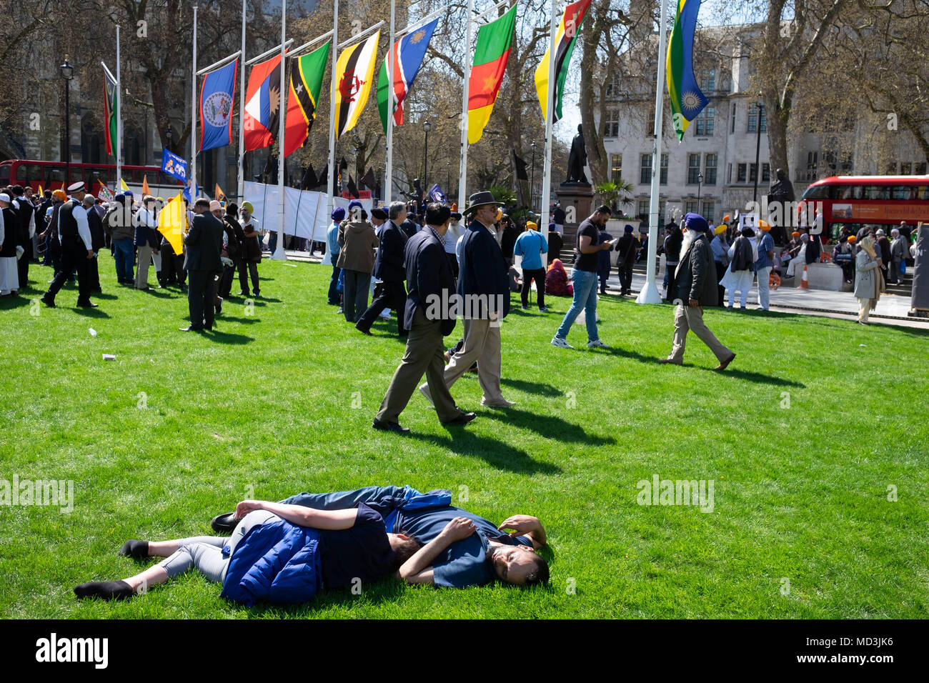 UK weather:   young couple fall asleep in the hot sunshine in Parliament Square in London, completely oblivious to the huge and very loud anti-Modi protest around them, on the hottest day of the year so far, Wednesday 18th April 2018 Stock Photo