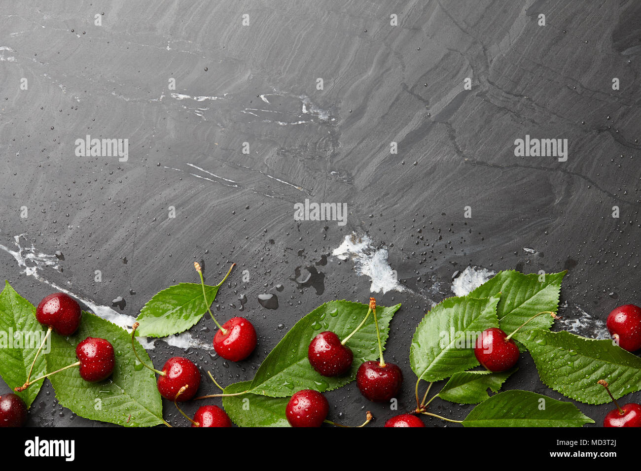 Frsh sweet cherries with leaves on black stone, top view Stock Photo