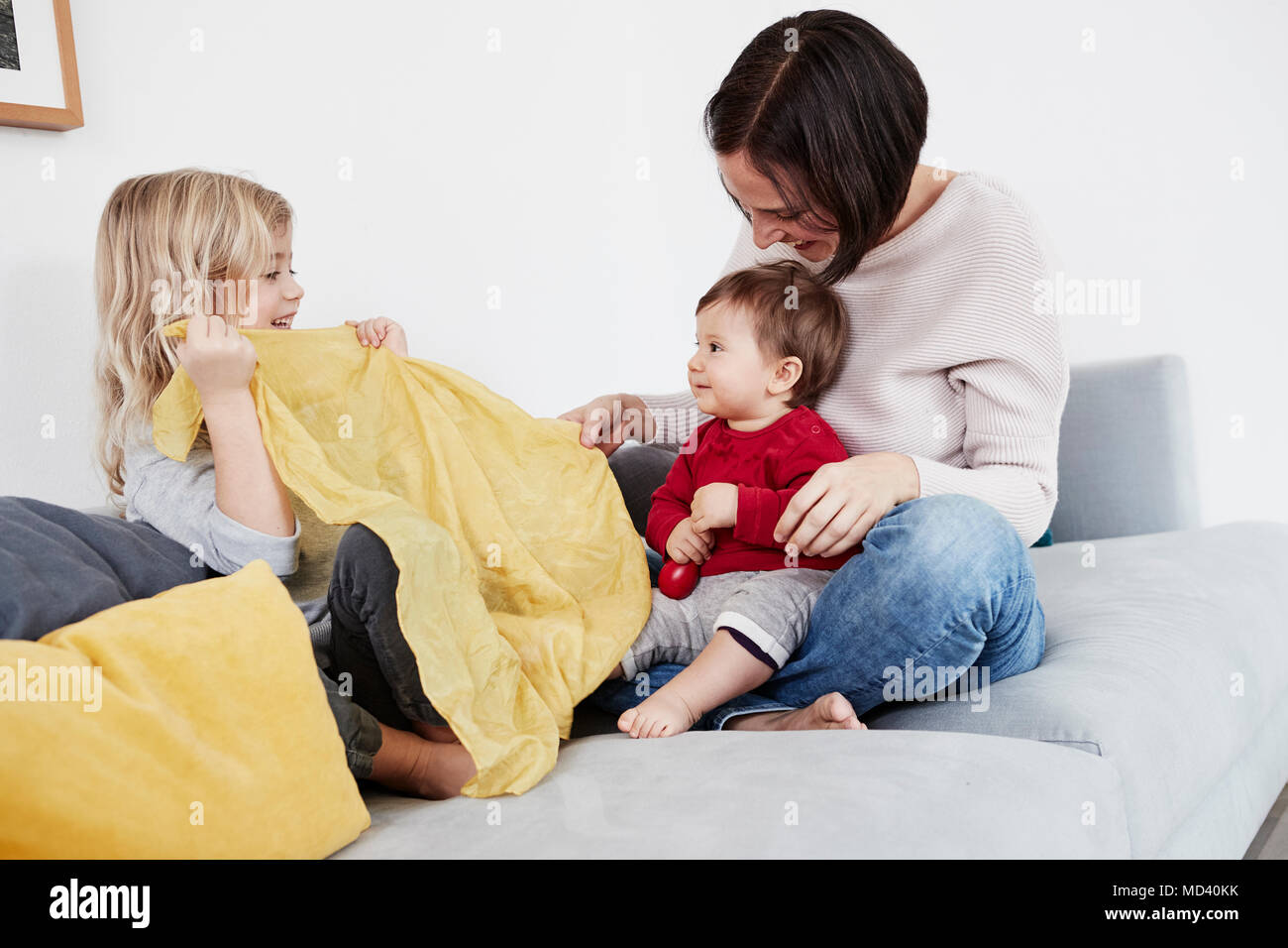 Family sitting on sofa, young girl playing peek-a-boo with baby sister Stock Photo