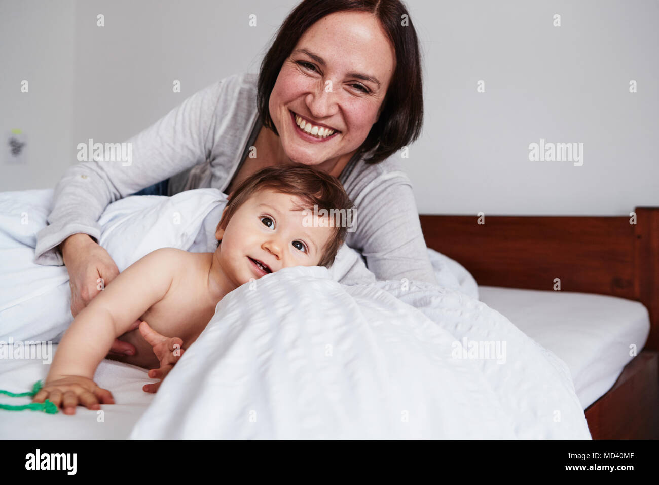 Mother and baby daughter relaxing on bed, smiling Stock Photo
