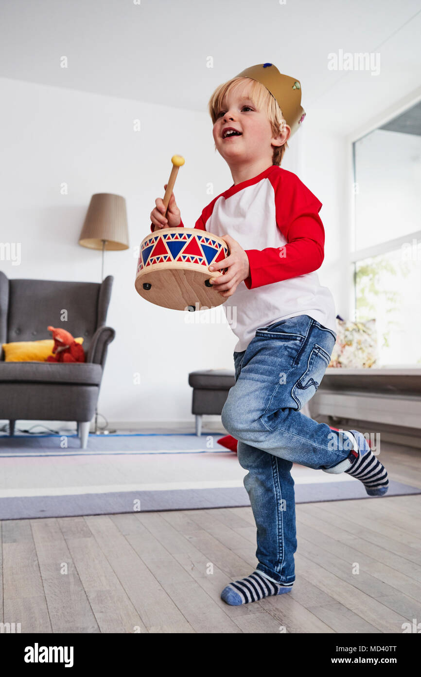 Young boy wearing cardboard crown, beating toy drum, low angle view Stock Photo
