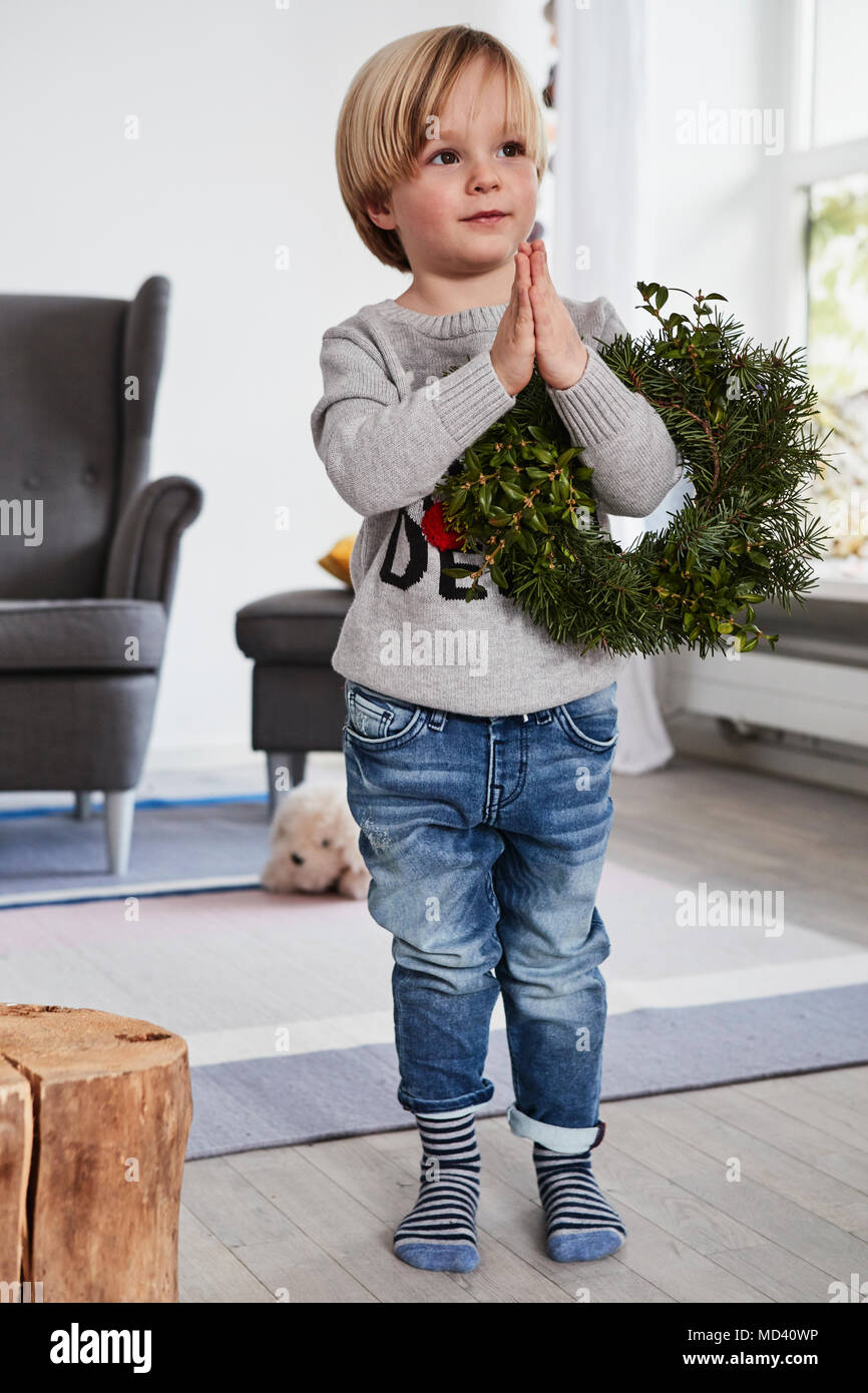 Young boy standing with hands together, holding wreath over arm Stock Photo