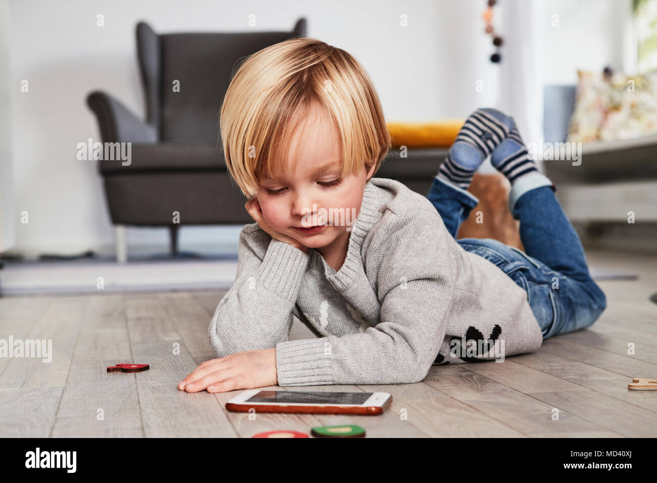 Young boy lying on floor,  using smartphone, looking at screen Stock Photo