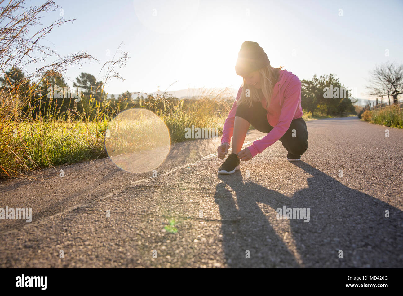Young woman exercising outdoors, tying shoelace Stock Photo