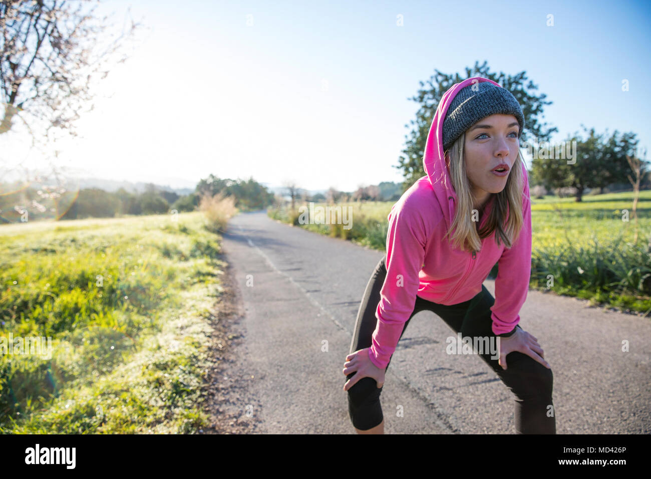 Young woman outdoors, taking a break from exercising, hands on knees Stock Photo