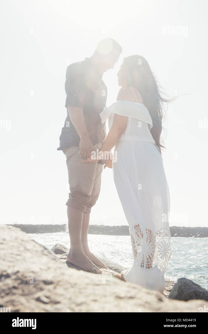 Couple standing on coastal rocks, holding hands, face to face, Seal