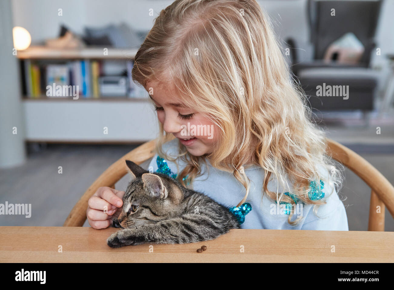 Portrait of young girl, sitting at table, stroking pet cat Stock Photo