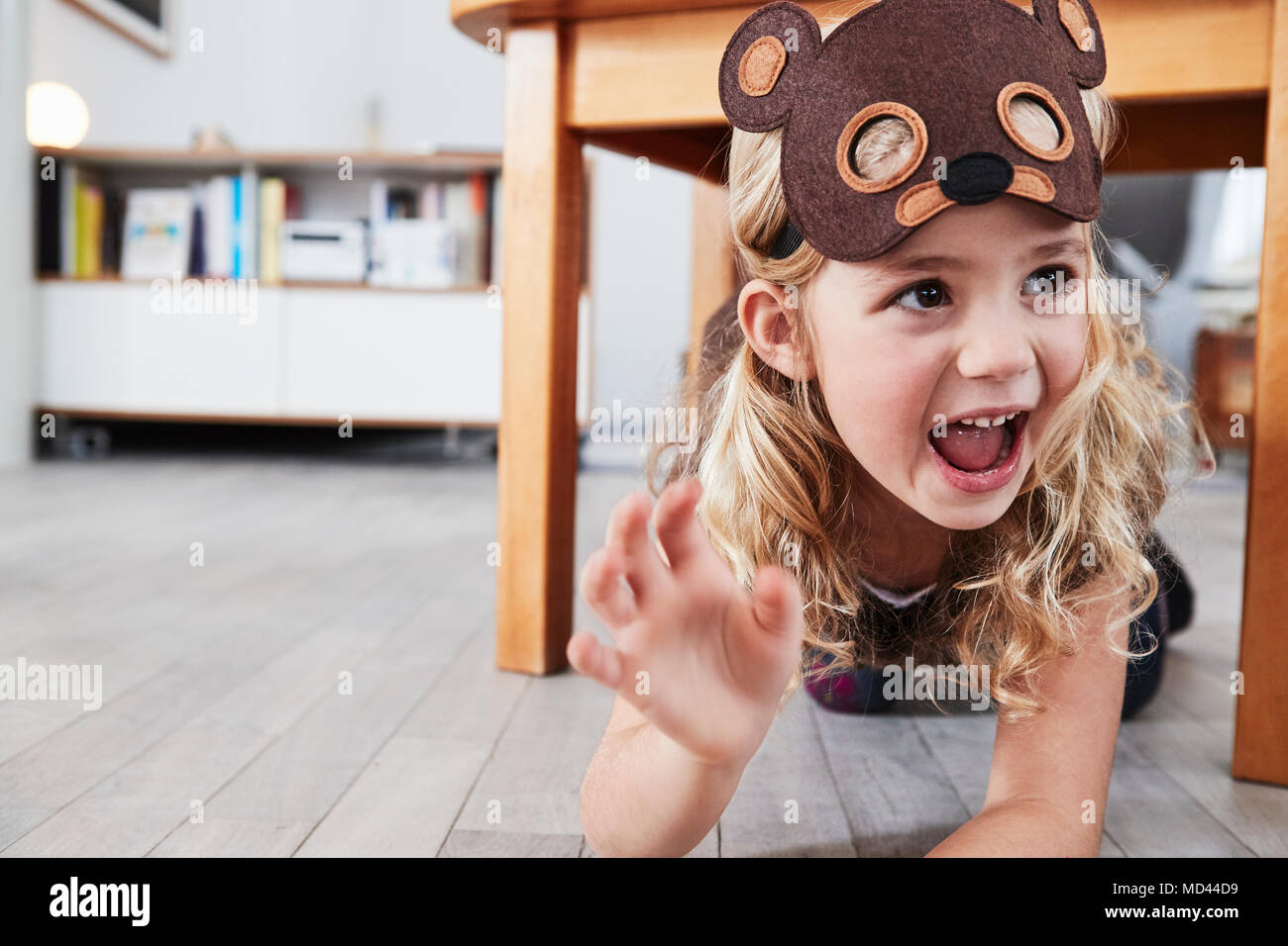 Young girl crawling under table, wearing bear mask, laughing Stock Photo