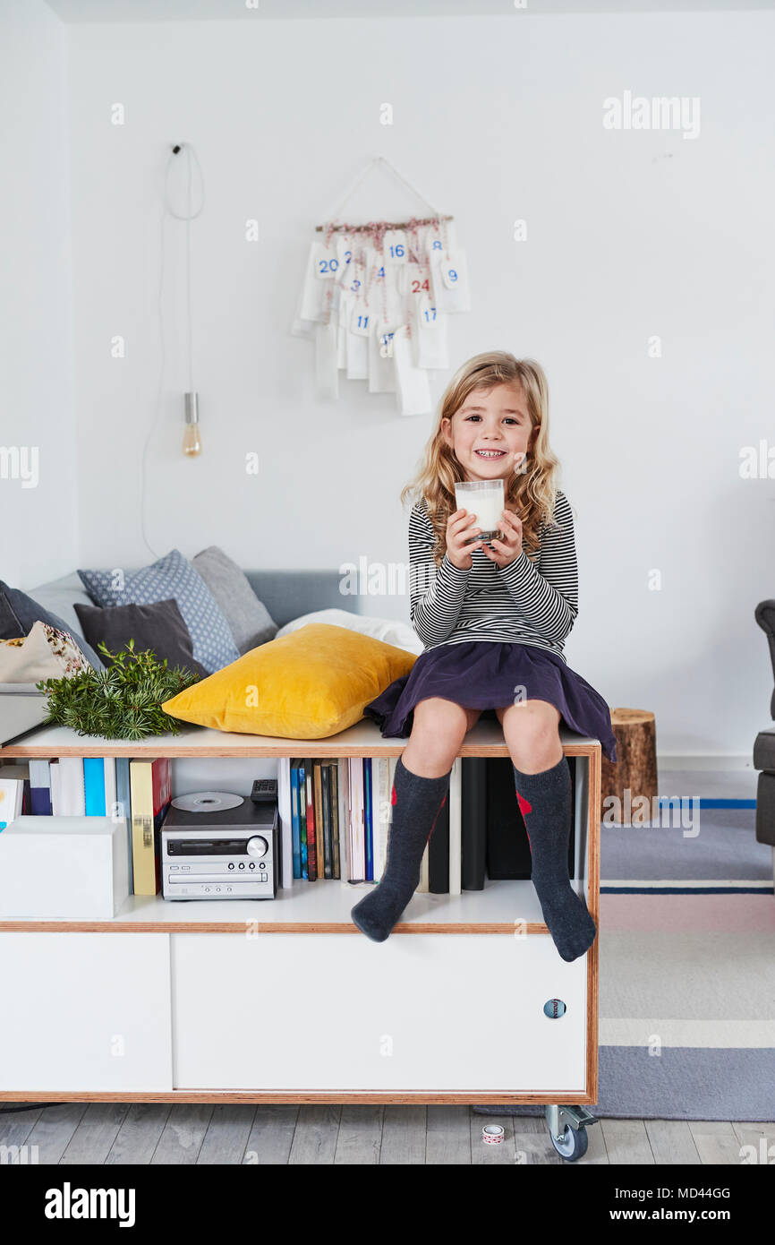 Young girl sitting in living room, holding glass of milk Stock Photo