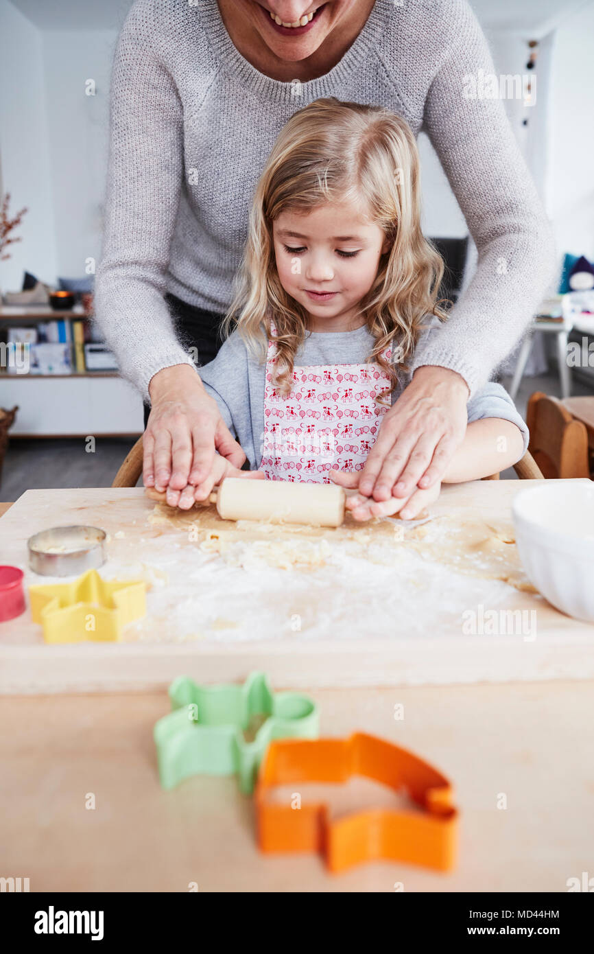 Mother helping daughter roll out cookie dough on kitchen table, mid section Stock Photo