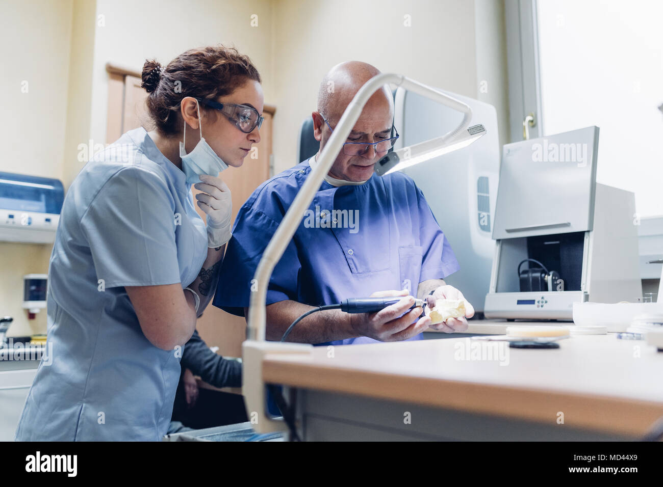 Dentist polishing denture in laboratory, female dentist watching
