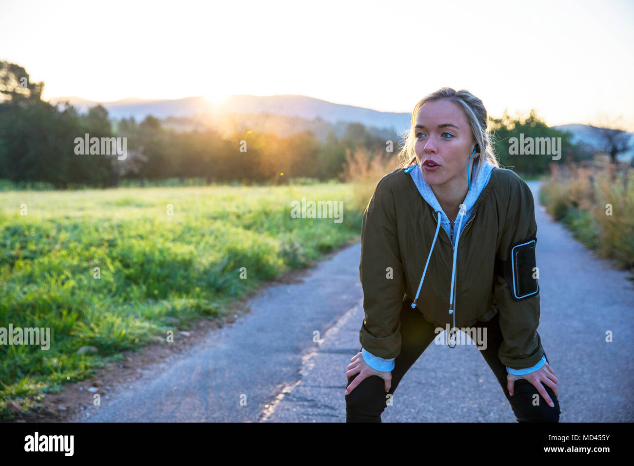 Young woman outdoors, taking a break from exercising, hands on knees Stock Photo