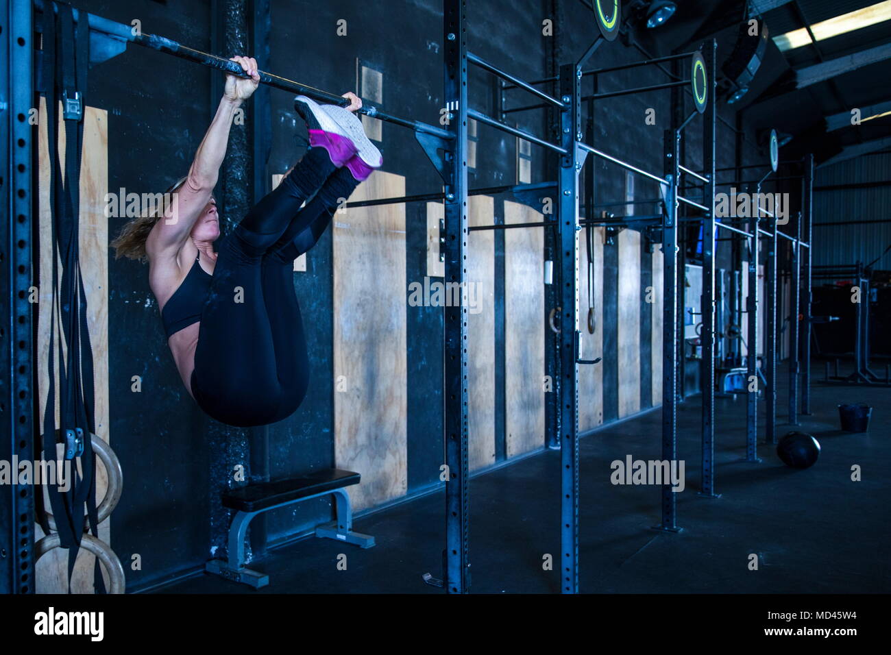 Woman exercising in gymnasium, using pull up bars Stock Photo