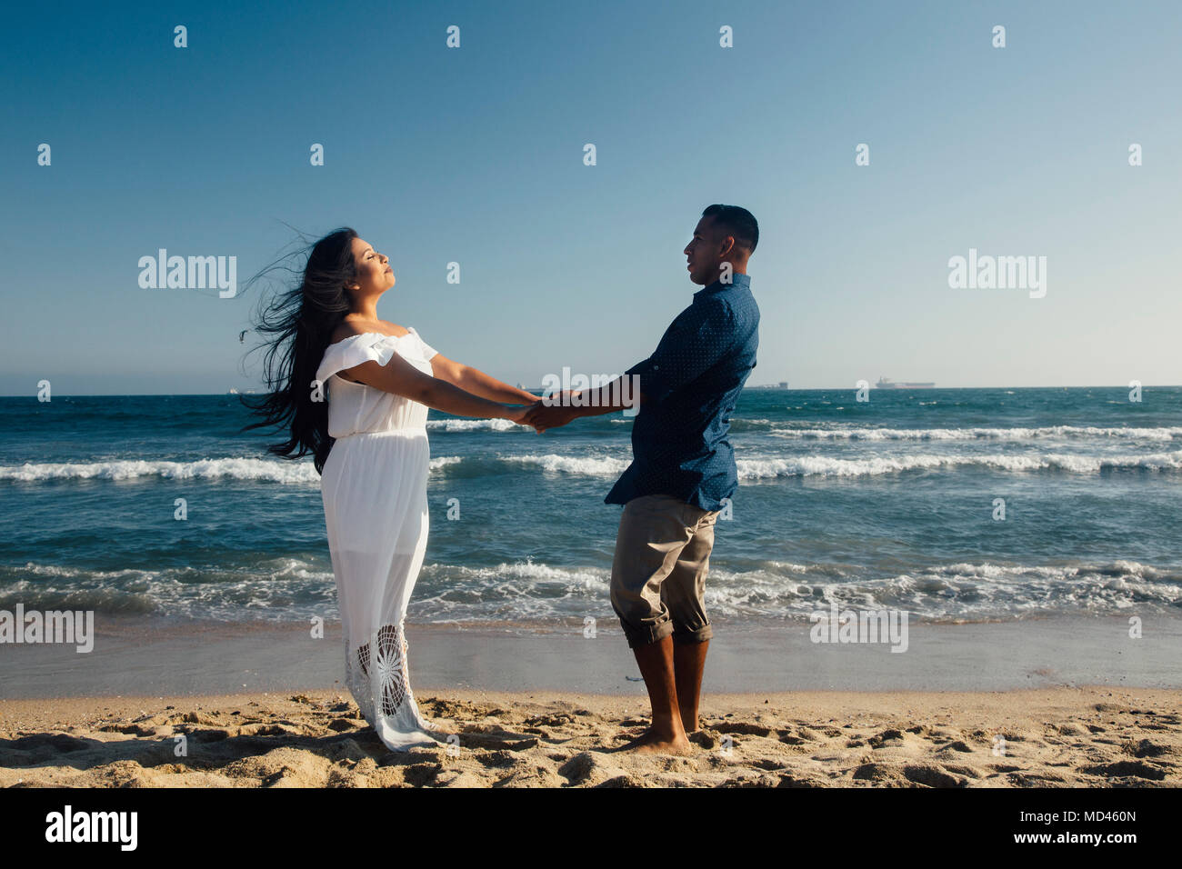 Couple standing on beach, holding hands, face to face, Seal Beach