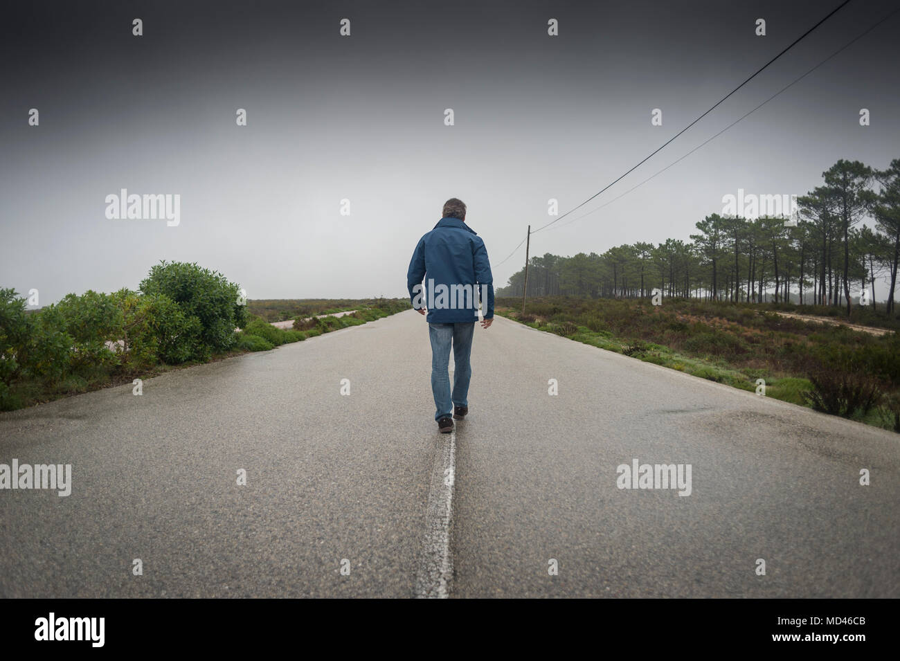 man walking along the centre of an empty road in the mist and fog Stock Photo