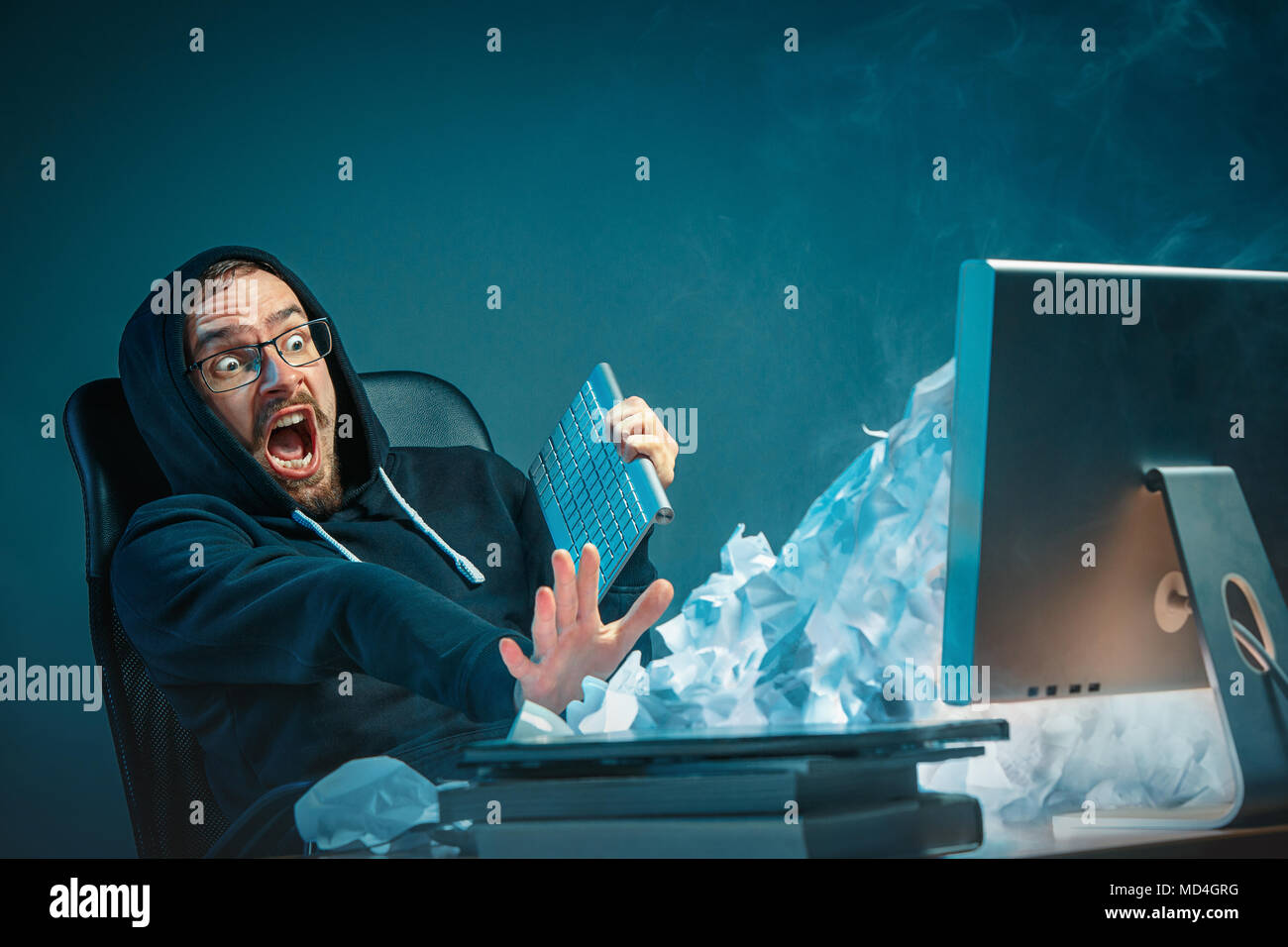 Young stressed handsome businessman working at desk in modern office shouting at laptop screen and being angry about spam Stock Photo