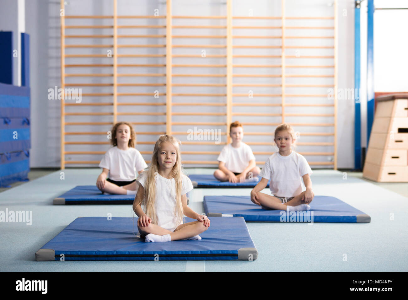 Kids sitting cross-legged on blue mats in the school gym Stock Photo