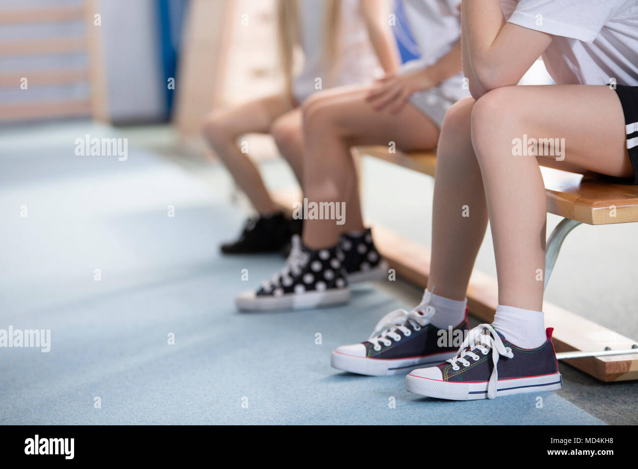 Cropped photo of children's legs in sneakers, sitting on a bench while waiting for a physical education class Stock Photo