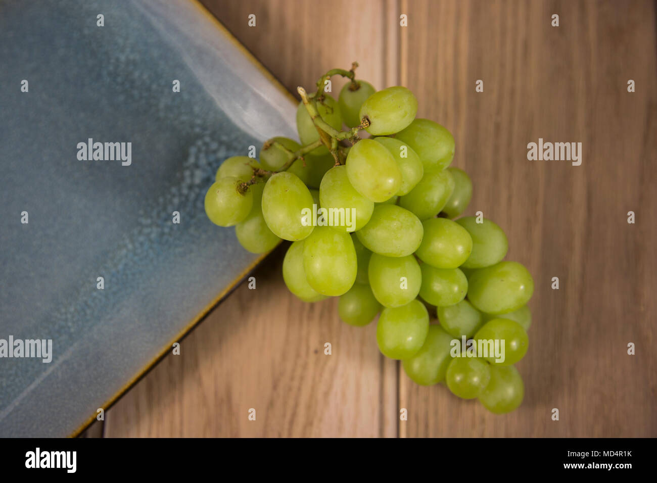 Flatlay from above  a bunch of green grapes by a blue plate on a wooden table Stock Photo