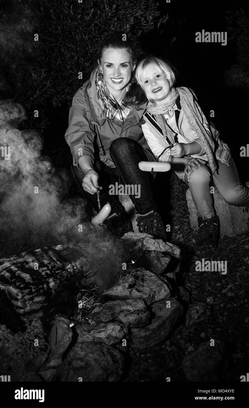 Into the wild. smiling young mother and daughter travellers near a campfire grilling sausages Stock Photo