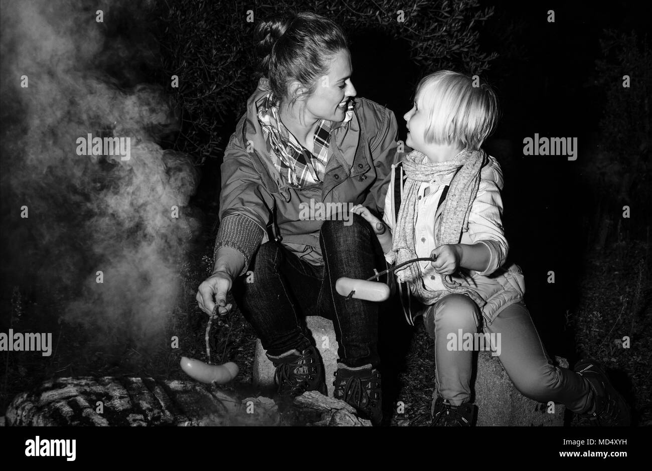 Into the wild. happy mother and child travellers near the camping fire grilling sausages Stock Photo