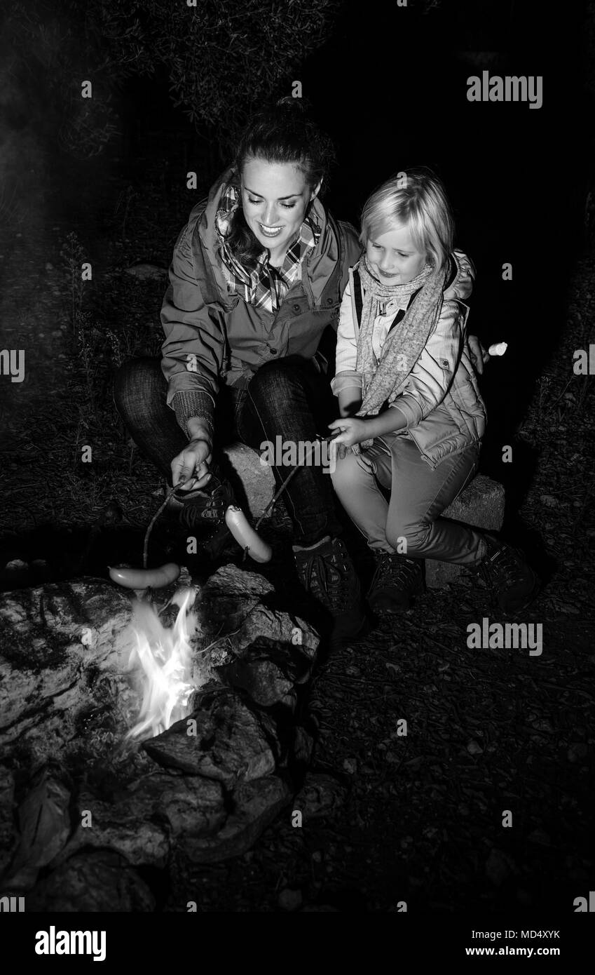 Into the wild. smiling healthy mother and daughter travellers near a bonfire grilling sausages Stock Photo