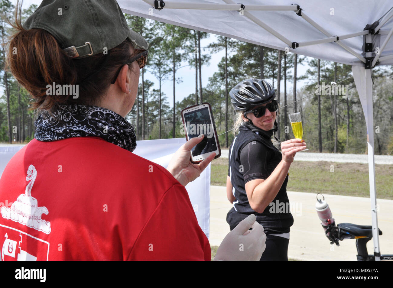 FORT BENNING, Ga. -- Stacey Thornhill, a paralegal assigned to the 316th Cavalary Brigade at Fort Benning, Georgia, takes a photo of a cyclist with a champagne flute of pickle juice at a rest stop sponsored by the 316th CAV during the Fort Benning Centennial Century Bike Ride at Columbus, Georgia, March 10, 2018. The 100-mile bike race, which leads cyclists through Fort Benning and downtown Columbus, takes place during the the year-long celebration of Fort Benning's 100th anniversary. (U.S. Army photo by Jessica Dupree/Released) Stock Photo