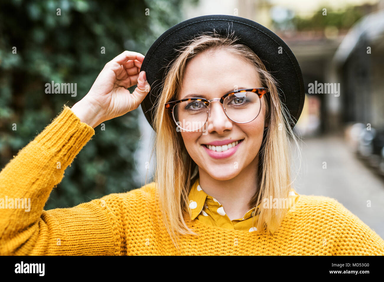 Young woman with black hat and glasses in sunny spring town. Stock Photo