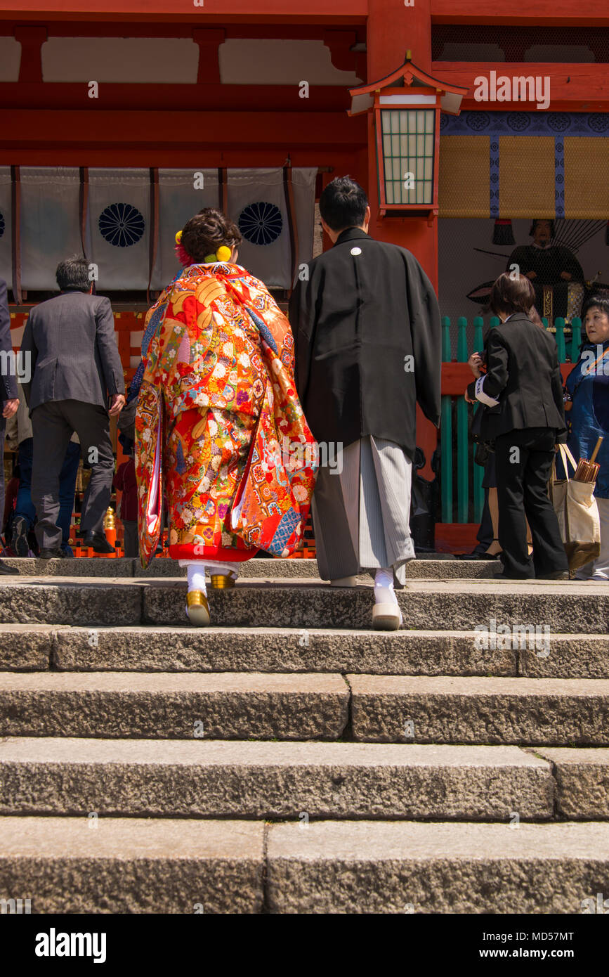 Couple in traditonal Japanese dress climb steps to shrine sheltered by parasol Stock Photo