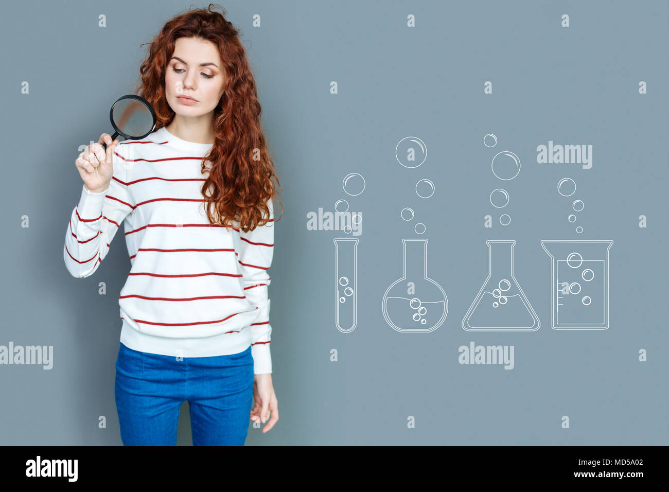 Clever scientist looking through the magnifying glass and feeling interested Stock Photo
