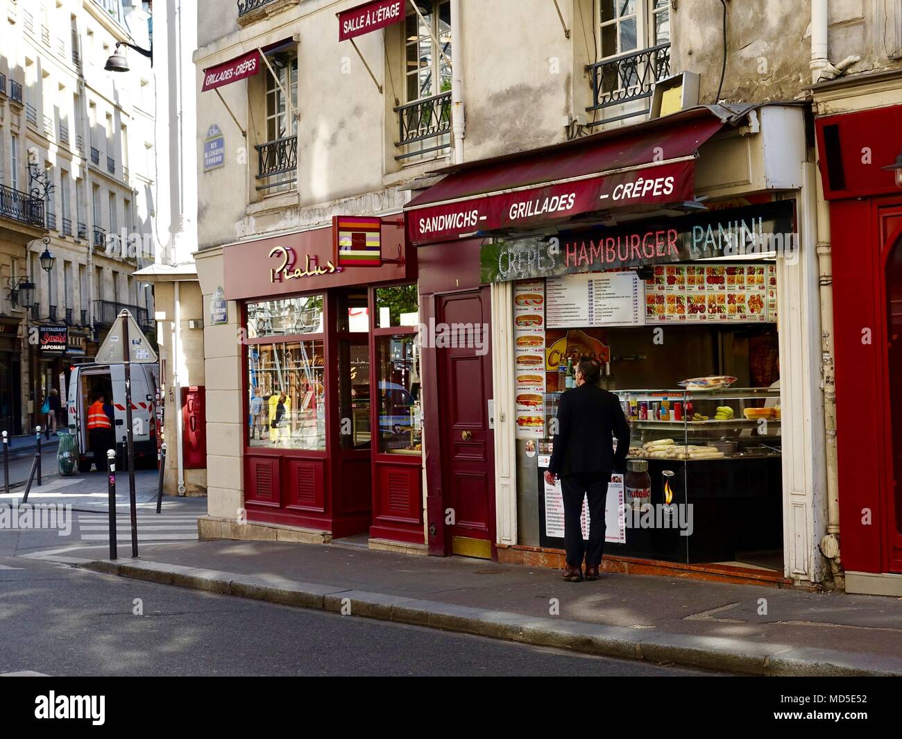 Man standing outside food shop featuring sandwiches, grilles, crepes, hamburgers, and panini in the 6th district, Paris, France Stock Photo