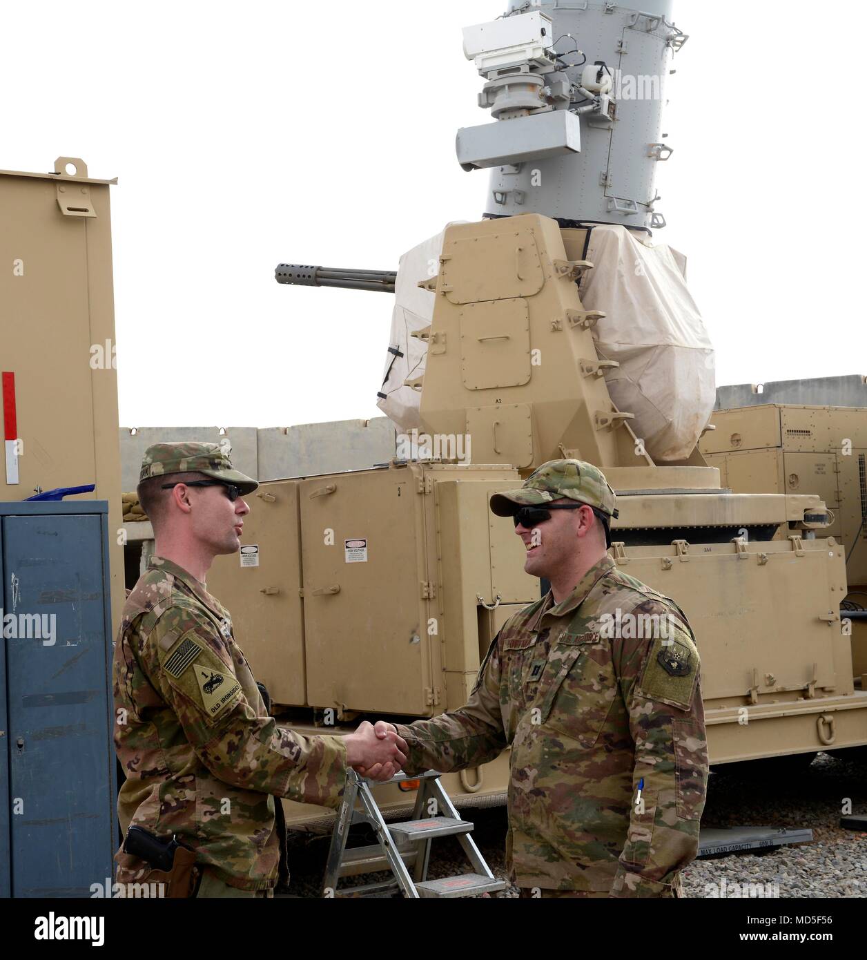 U.S. Army Capt. Eric Sylwestrak, battery commander, 2nd Battalion, 174th Air Defense Artillery Regiment, Ohio Army National Guard, shakes hands with U.S. Air Force Capt. Isaac Hoffman, project engineering officer-in-charge, 220th Engineering Installation Squadron, Ohio Air National Guard, in front of one of the Army's Counter-Rocket, Artillery, and Mortar (C-RAM) Intercept weapon systems at Kandahar Airfield, Afghanistan, March 10, 2018.  Airmen and Soldiers with both Ohio National Guard units worked together throughout a significant portion of their deployment during the past few months to co Stock Photo