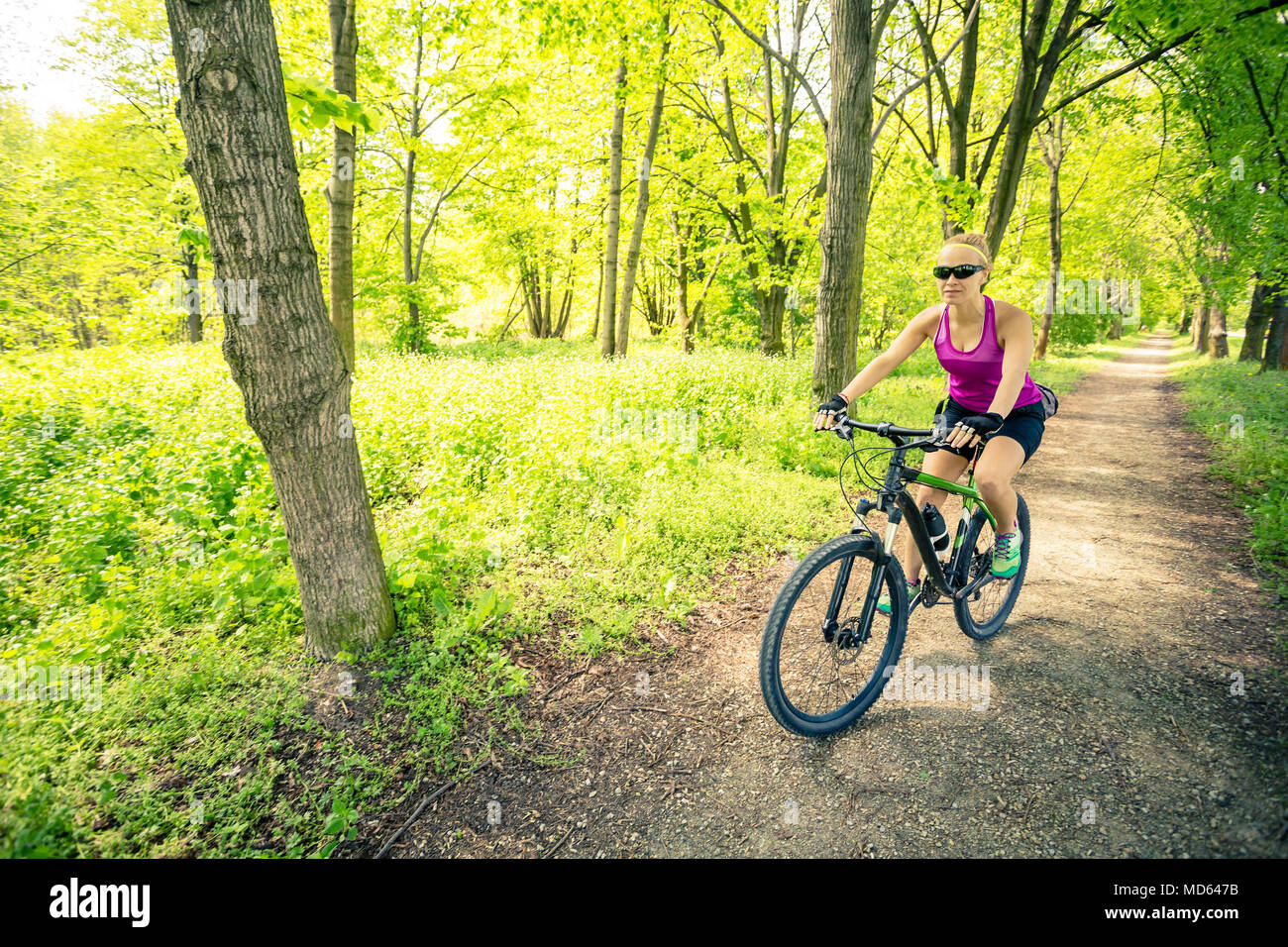 Woman cycling a mountain bike in a city park, summer day. Inspire and motivate concept for outdoors activity. Girl cyclist smiling and riding bicycle  Stock Photo