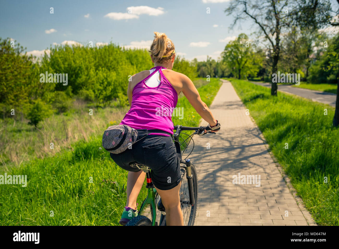 Woman cycling a mountain bike in a city park, summer day. Inspire and motivate concept for outdoors activity. Girl cyclist smiling and riding bicycle  Stock Photo