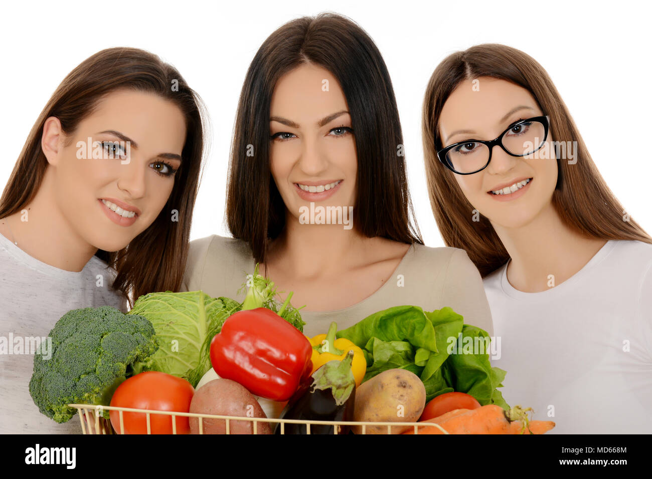 Three beautiful girls holding basket full of mixed vegetables Stock Photo