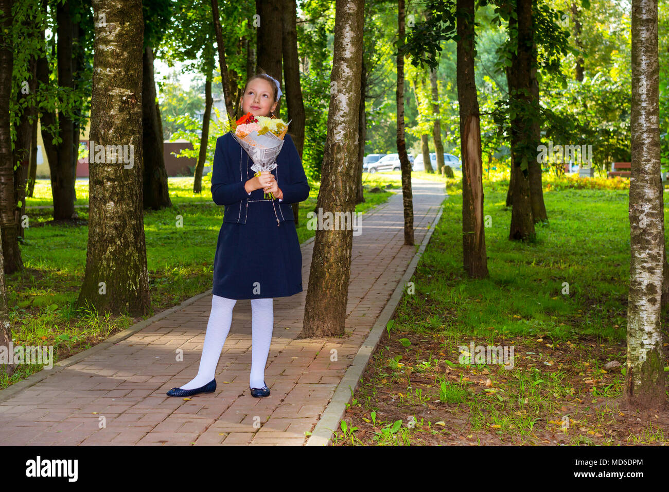 Little first-grader, girl student goes to school on knowledge day 1. September. Student of elementary school in uniform with flowers posing in autumn  Stock Photo
