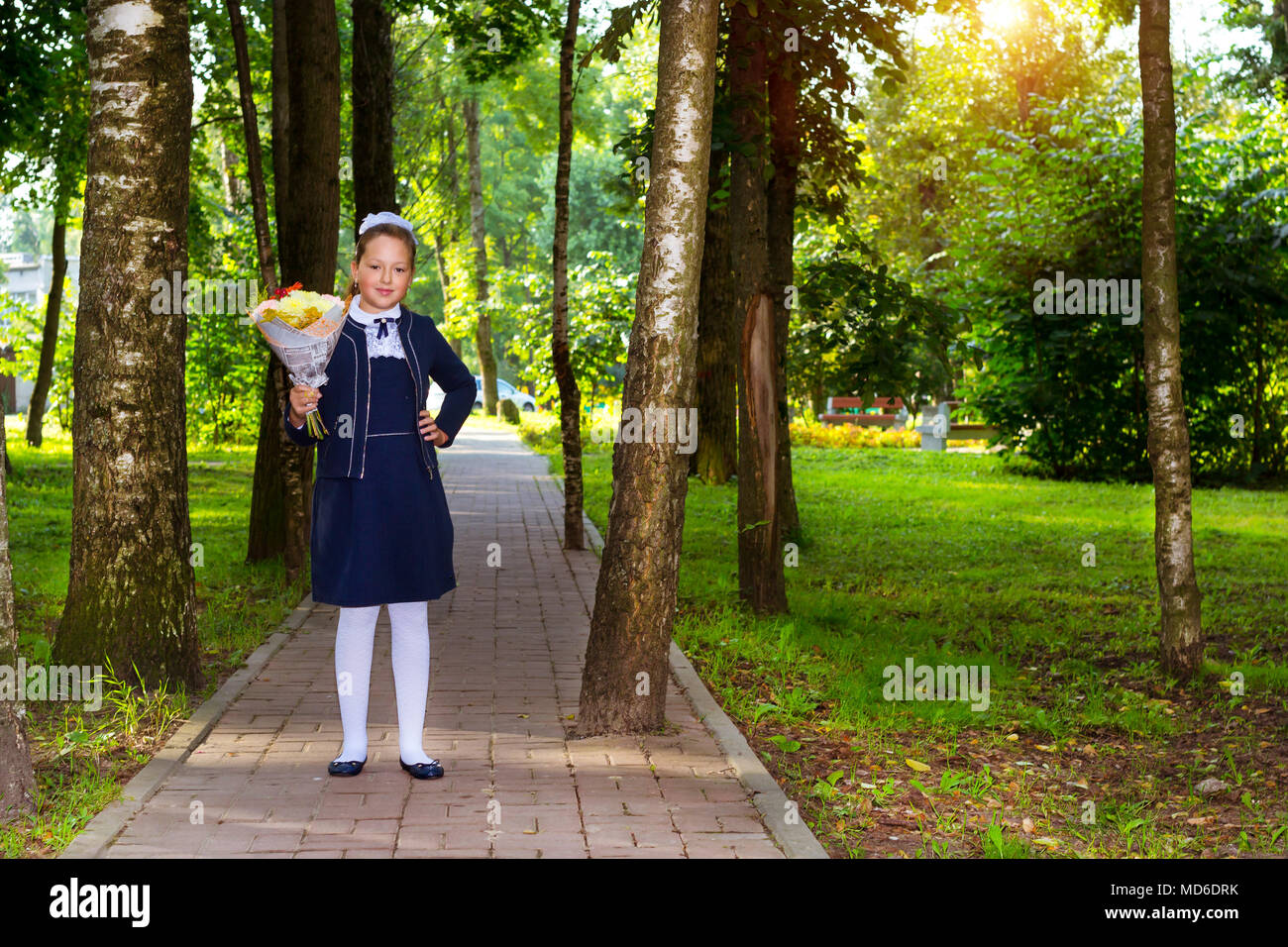 Little first-grader, girl student goes to school on knowledge day 1. September. Student of elementary school in uniform with flowers posing in autumn  Stock Photo