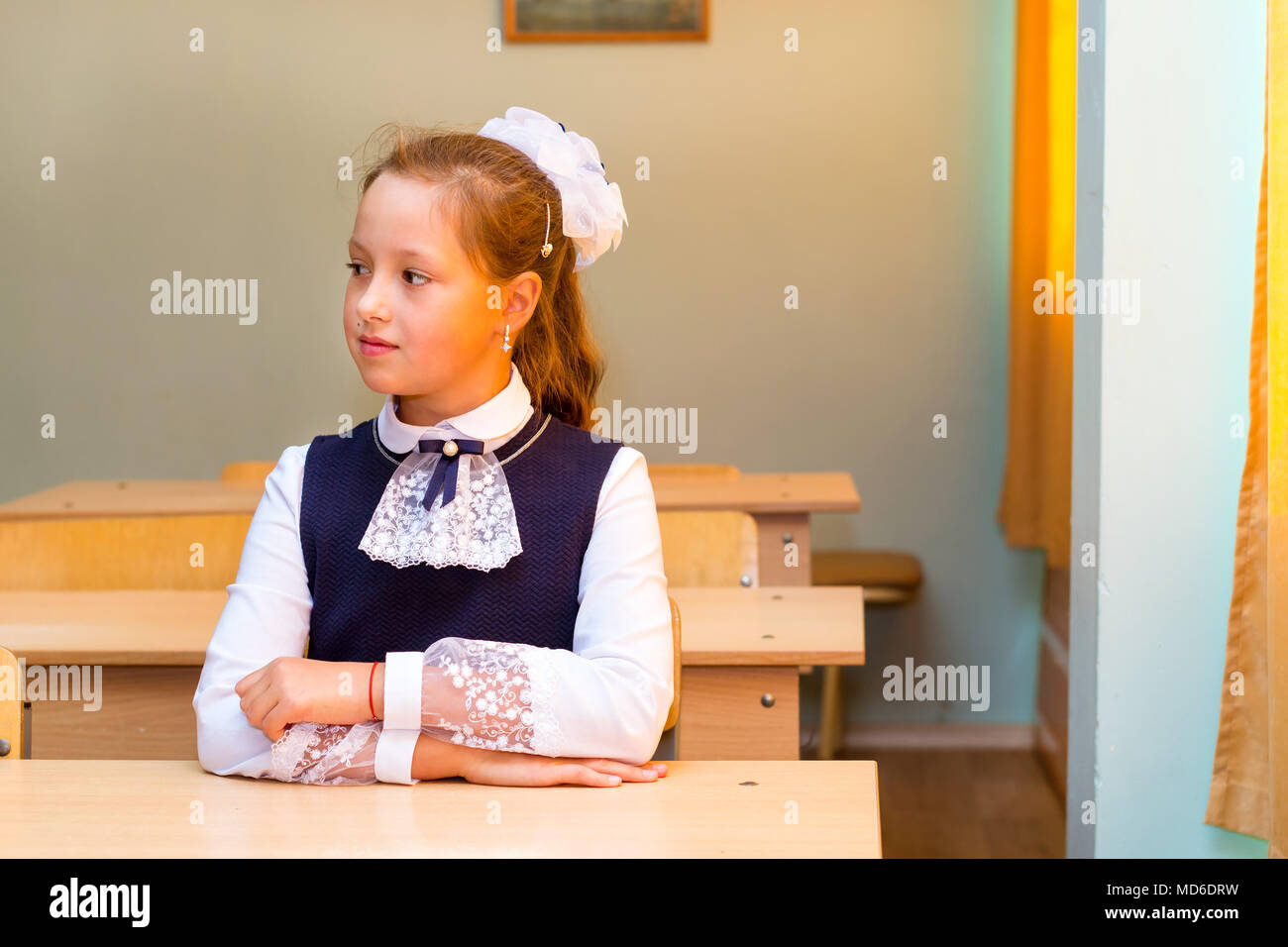 Little first-grader, girl-student in school on knowledge day - 1. September. Student of elementary school in uniform with bows posing in classroom. Ed Stock Photo