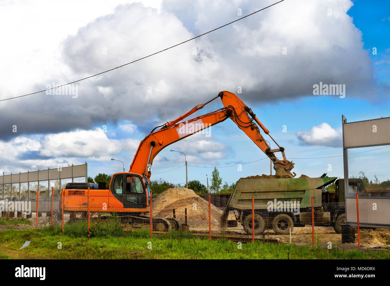 Excavator bucket loads heavy truck with ground on construction of highspeed road around Krasnoe Selo. Heavy industry machinery equipment for excavatio Stock Photo