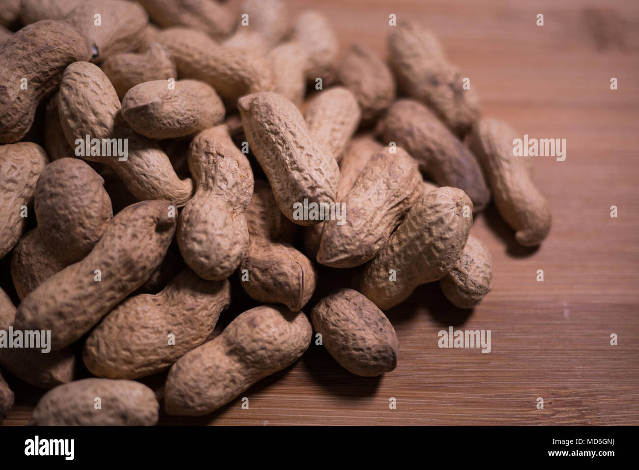Pile of unshelled natural peanuts in the shell on a wooden grained background and natural light with shadows. Stock Photo