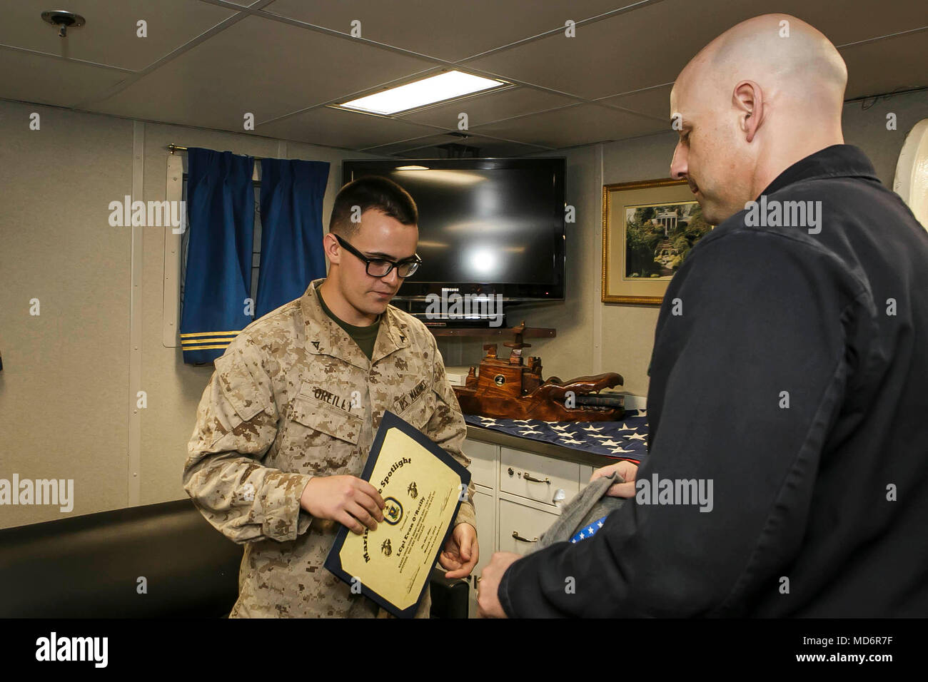 U.S. 5TH FLEET AREA OF OPERATIONS (March 31, 2018) Marine Corps Lance Cpl. Evan O'Reilly, left, 20, a native of Gardner, Massachusetts and team member assigned to Fox Company, Battalion Landing Team, 2nd Battalion, 6th Marine Regiment, 26th Marine Expeditionary Unit, receives the Marine in the Spotlight award from Cmdr. Philip Knight, right, commanding officer of the Harpers Ferry-class dock landing ship USS Oak Hill (LSD 51) aboard ship. The Oak Hill is deployed to the U.S. 5th Fleet area of operations in support of maritime security operations to reassure allies and partners and preserve the Stock Photo