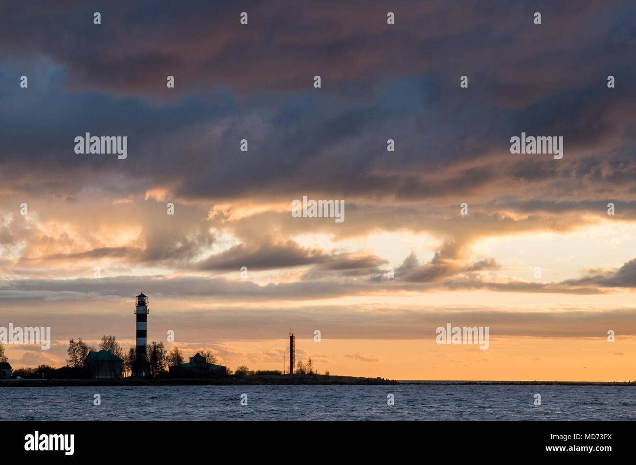 Beautiful clouds in warm light of a setting sun over a lighthouse on a seaside. Stock Photo