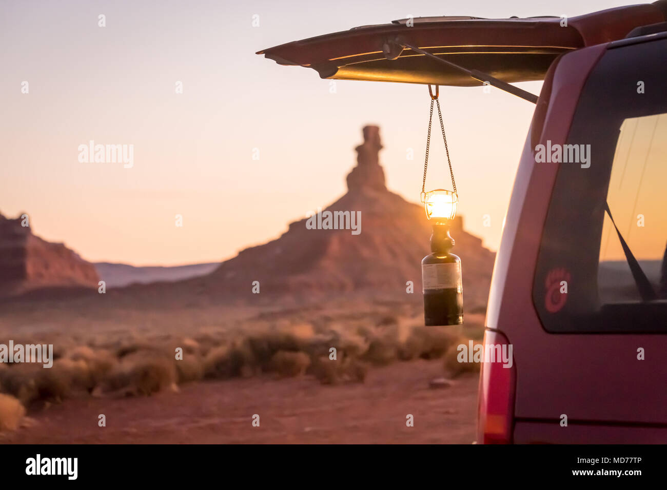 A glowing lantern hangs from the back door of a red SUV in the desert of southern Utah. Stock Photo