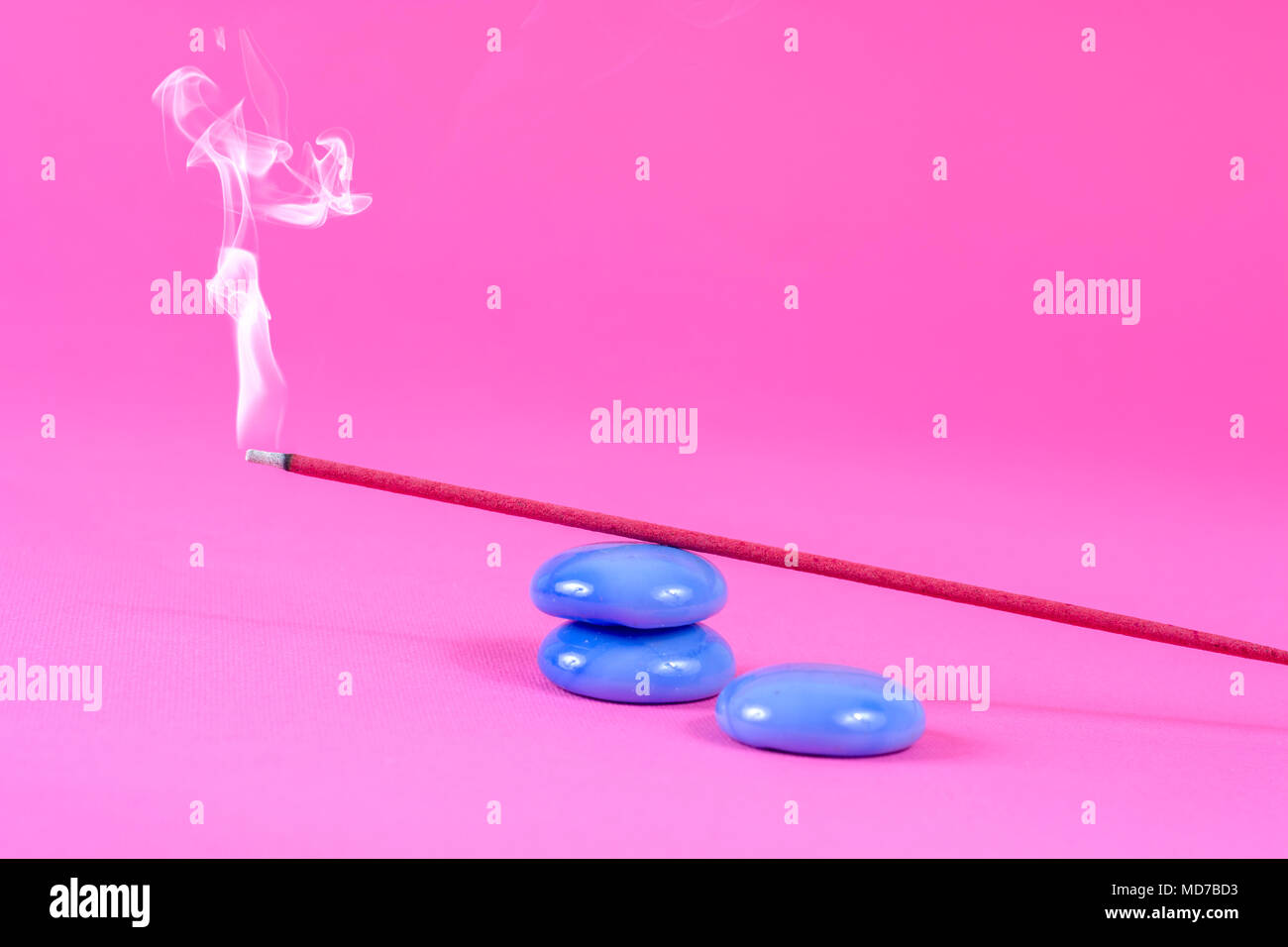 Incense stick burning and smoke on blue rock on pink background in