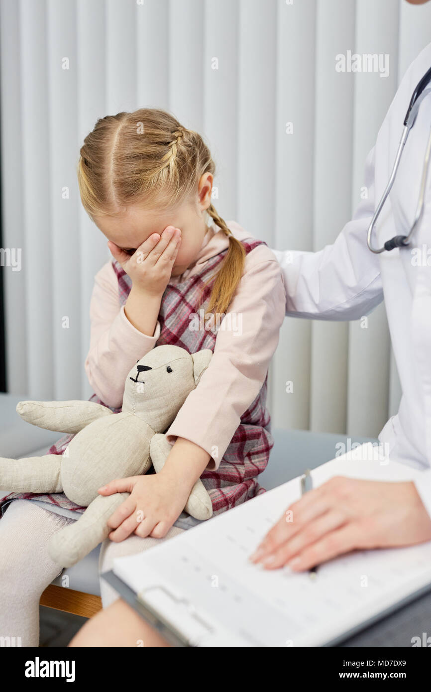 Little girl crying at hospital with doctor sitting nearby Stock Photo